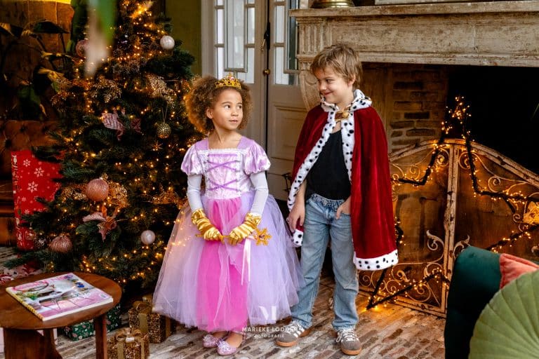 Jongen draagt de rode King Louis cape met witte kraag en bontrand met zwarte stippen naast een meisje in prinsessenjurk.