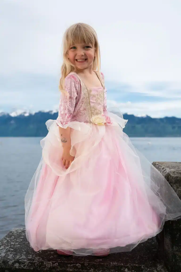 Meisje draagt een roze prinsessenjurk met hoepel, gouden details en een zeer wijde tule rok aan het water