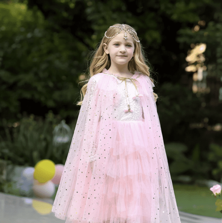 Meisje draagt een roze prinsessencape van tule met goudkleurige sterren in een groene tuin