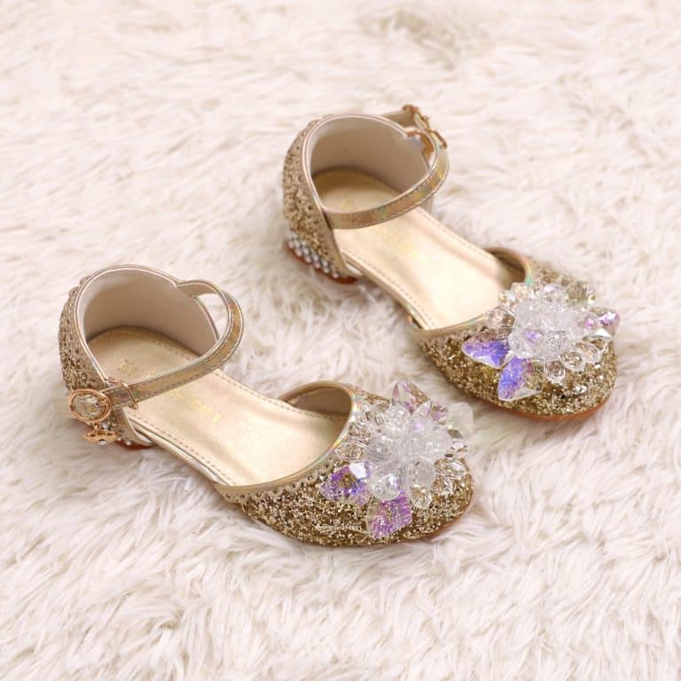 Gouden prinsessenschoenen met hakjes en enkelbandjes, versierd met grote glinsterende bloemen en paarse steentjes.