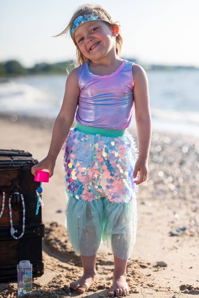 Meisje draagt de paarse paillettenrok met turquoise tailleband en haaraccessoire op het strand.