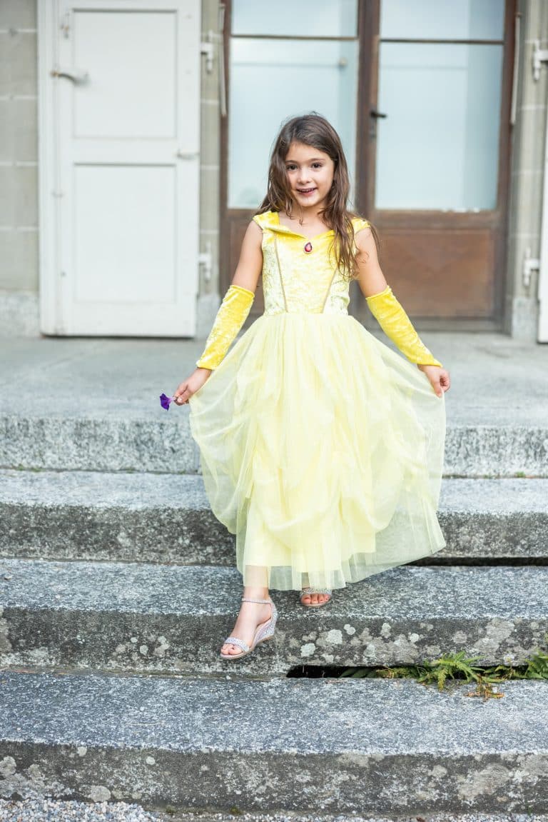 Meisje draagt een gele Belle prinsessenjurk met lange handschoenen en een glinsterende rok op de traptreden.