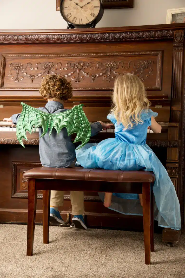 Jongen draagt de groene drakenvleugels van de drakenvleugels- en maskerset naast een meisje aan de piano.