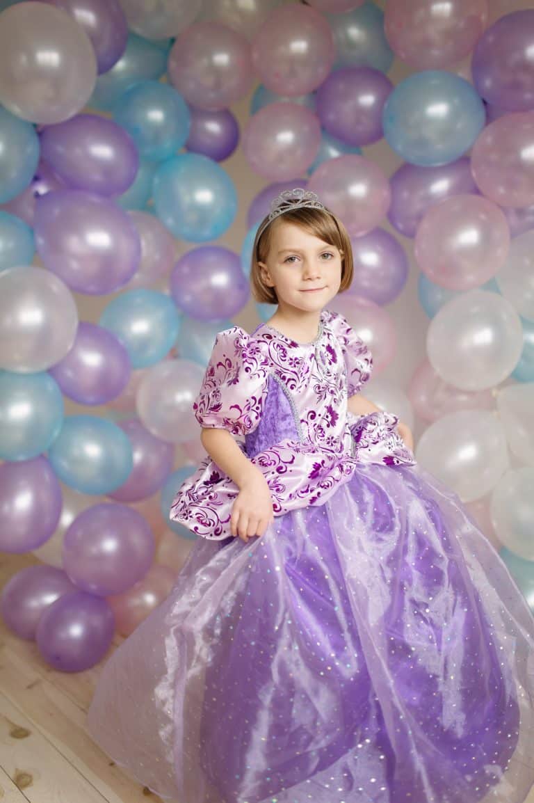 Meisje draagt de paarse Rapunzel prinsessenjurk van Great Pretenders met sierlijk patroon, tule rok en tiara voor ballonnen.