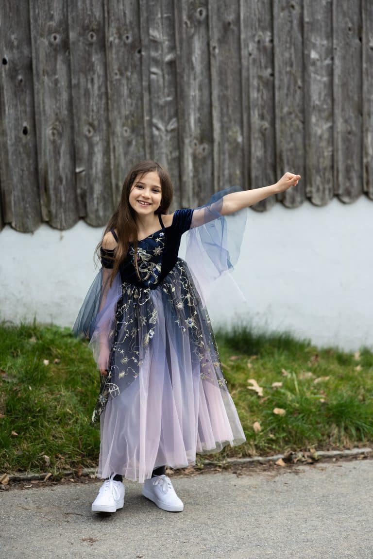 Meisje draagt de blauwe Enchantress Gown met transparante mouwen en tule rok met sterren- en maanborduursels