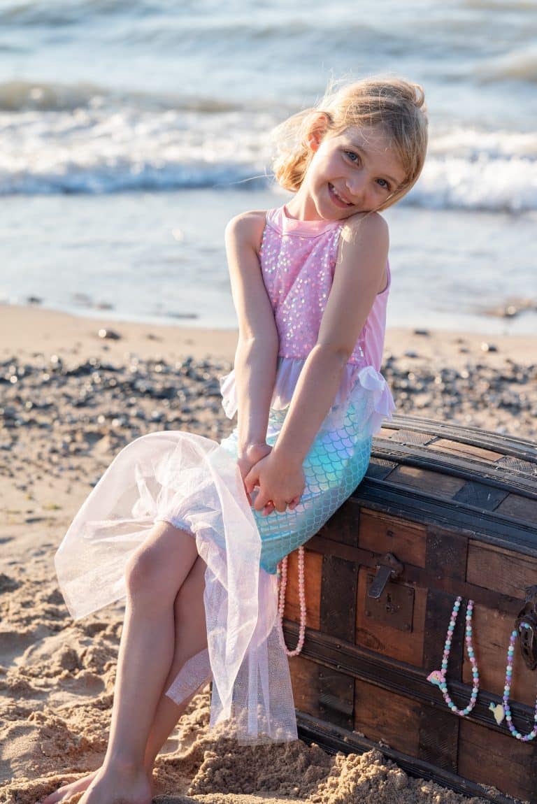 Meisje draagt een roze zeemeermin verkleedjurk met glanzende top, zeegroene schubbenrok en tule zoom op het strand