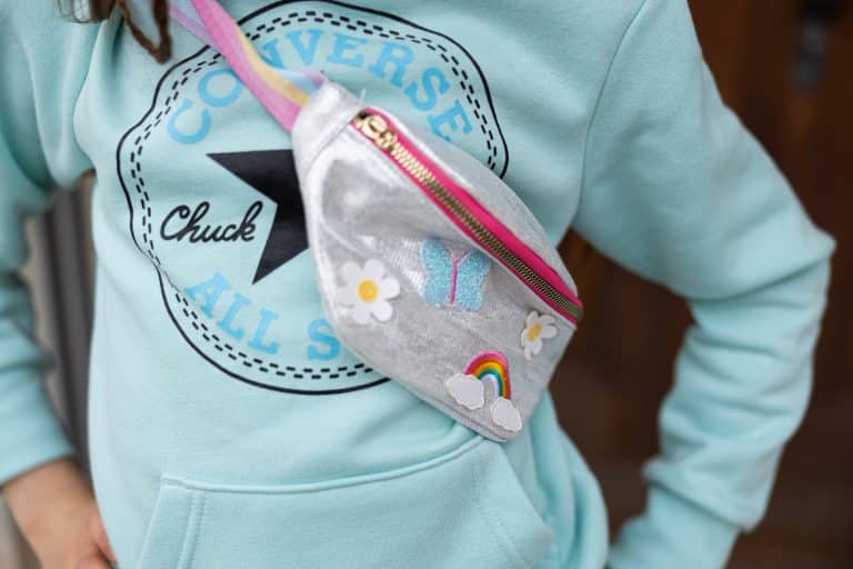 Meisje draagt een regenboog Unicorn schoudertas, een meisjes tas met roze rits en geborduurde bloemen en regenboog.