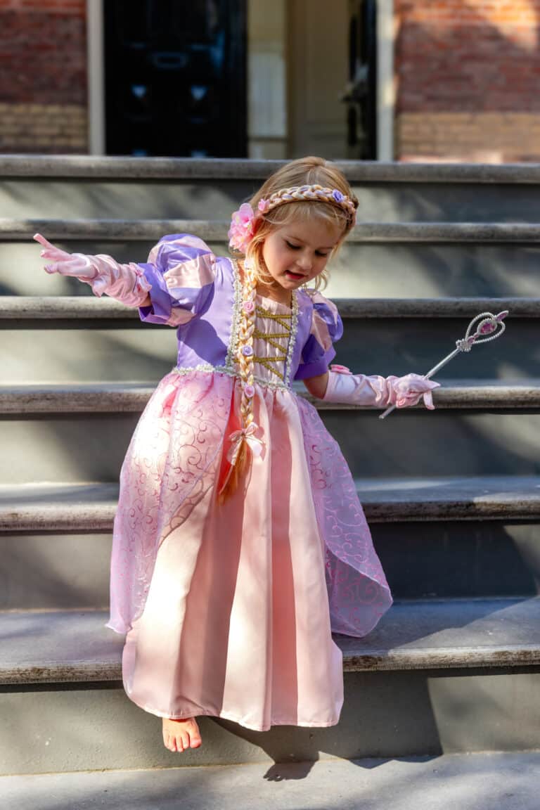 Meisje draagt een paarse prinsessenjurk van Rapunzel met roze rok, lange vlecht, handschoenen en toverstaf op de trap