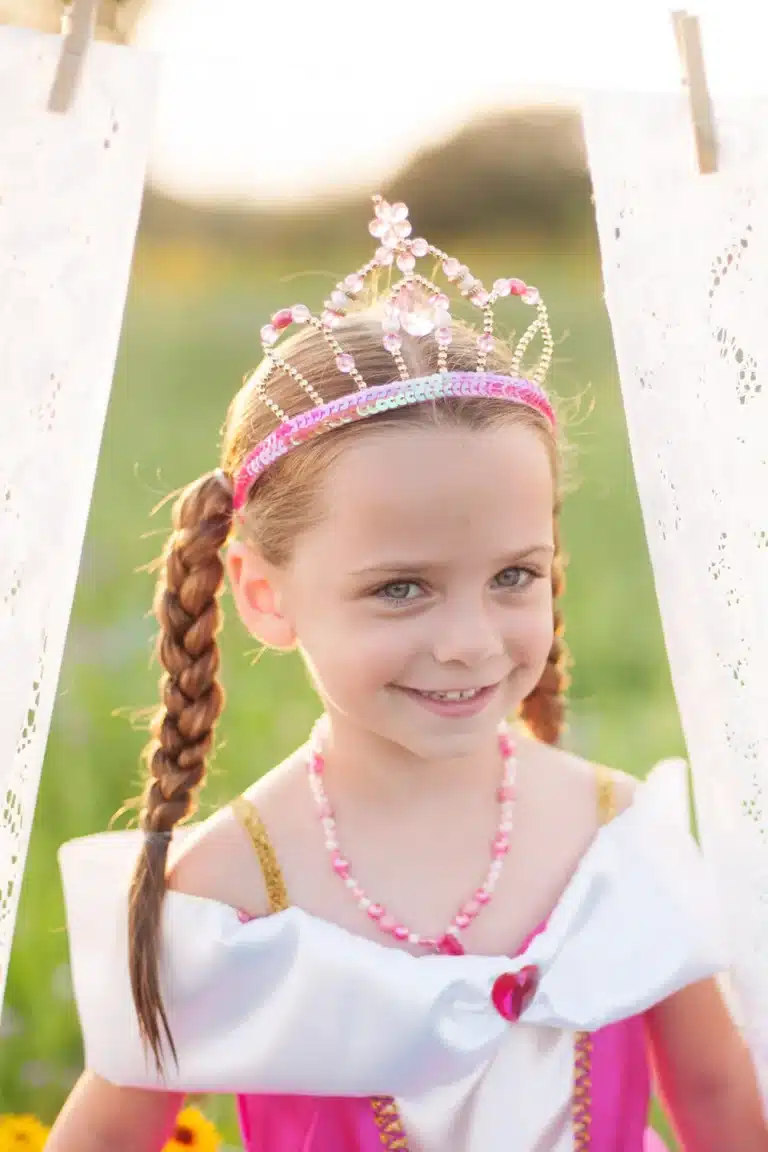 Meisje draagt een roze Great Pretenders tiara met fonkelende steentjes en gouden kralen bij een roze prinsessenjurk.